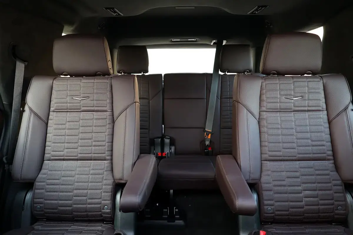 The interior image appears to show the rear passenger seating configuration of a Cadillac Escalade featuring brown leather captain's chairs in the second row and a bench seat in the third row.
